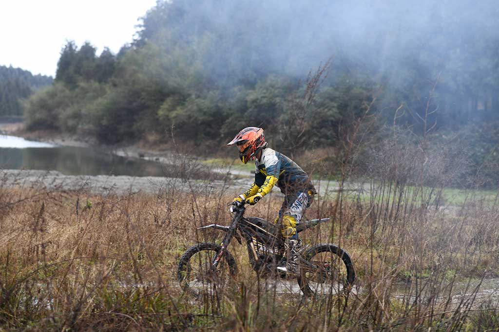 Talaria sähkömopolla ajava kuljettaja sumuisessa maastossa ja mutaisella polulla.